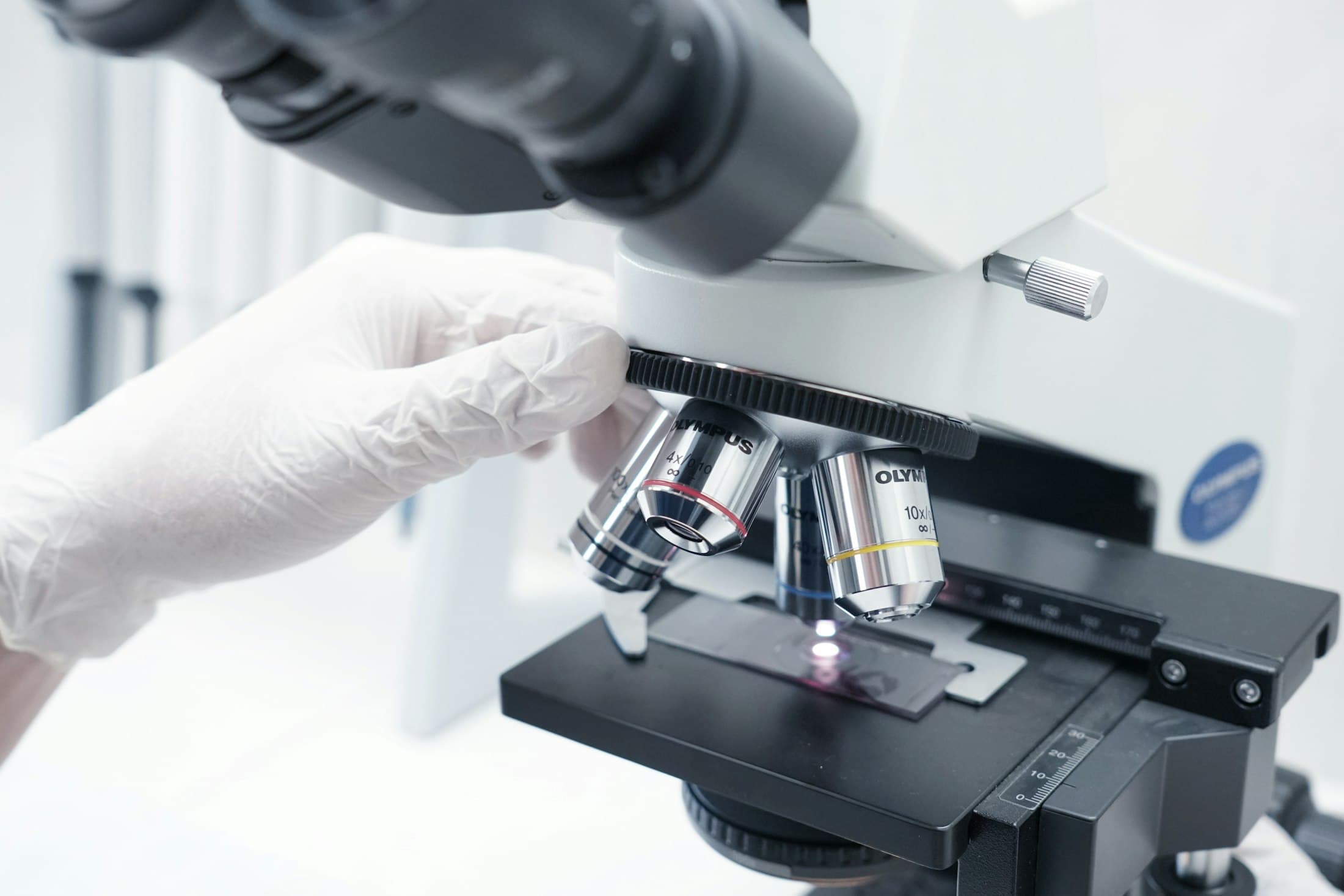 A gloved hand placing a slide under a microscope