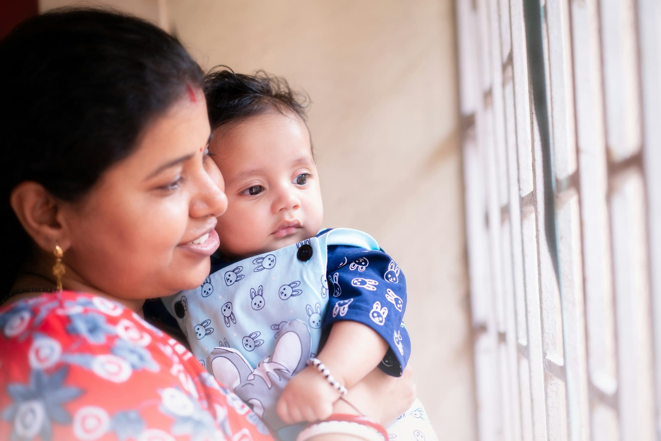 A mother holding her baby by a window